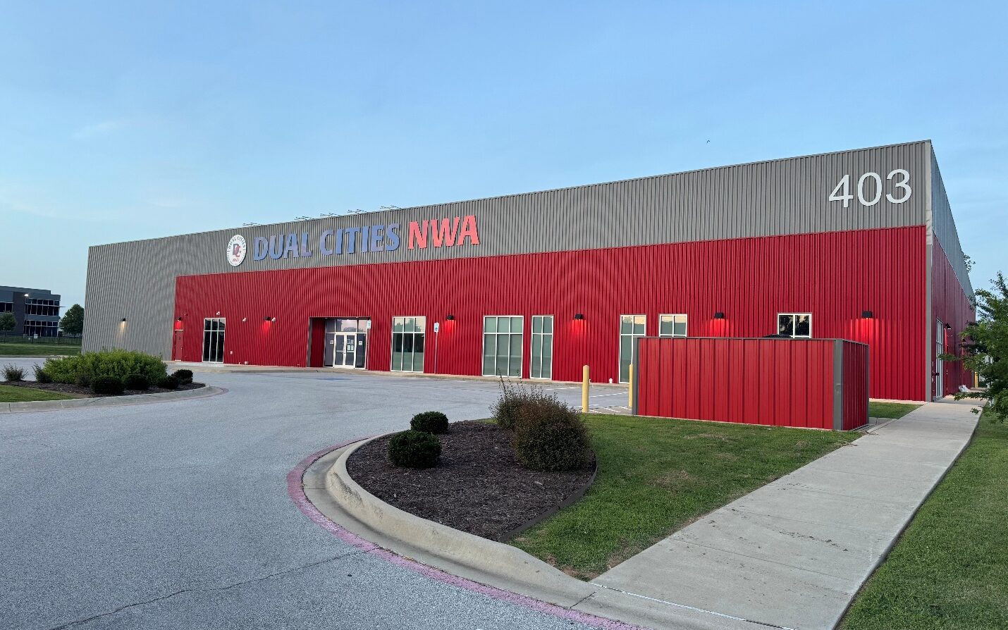 The red Dual Cities NWA building at dusk, sign over the entrance and the 403 address on the corner.