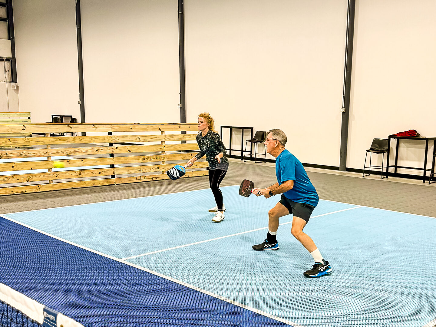 Two players in a rally on an indoor pickleball court at Dual Cities NWA.